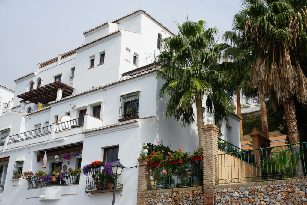 Elegant white villa surrounded by palm trees and vibrant flowers, showcasing Spanish architecture.